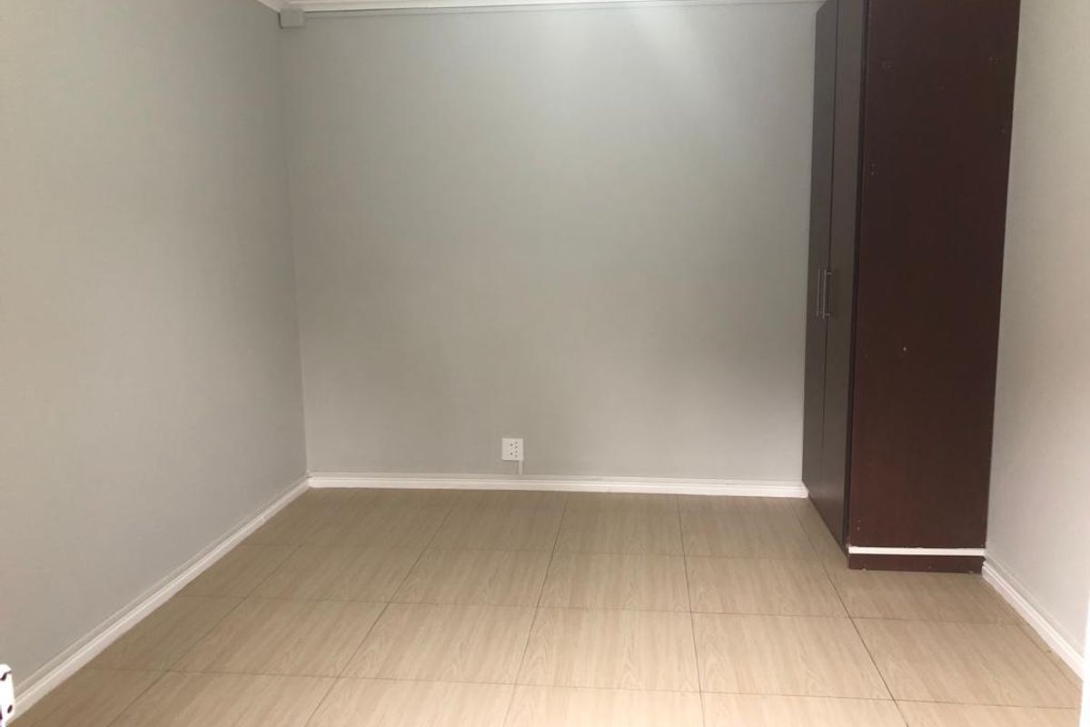 A clean, empty bedroom featuring neutral grey walls, light wood-look tiled flooring, and a built-in dark wood cupboard.