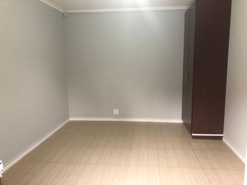 A clean, empty bedroom featuring neutral grey walls, light wood-look tiled flooring, and a built-in dark wood cupboard.