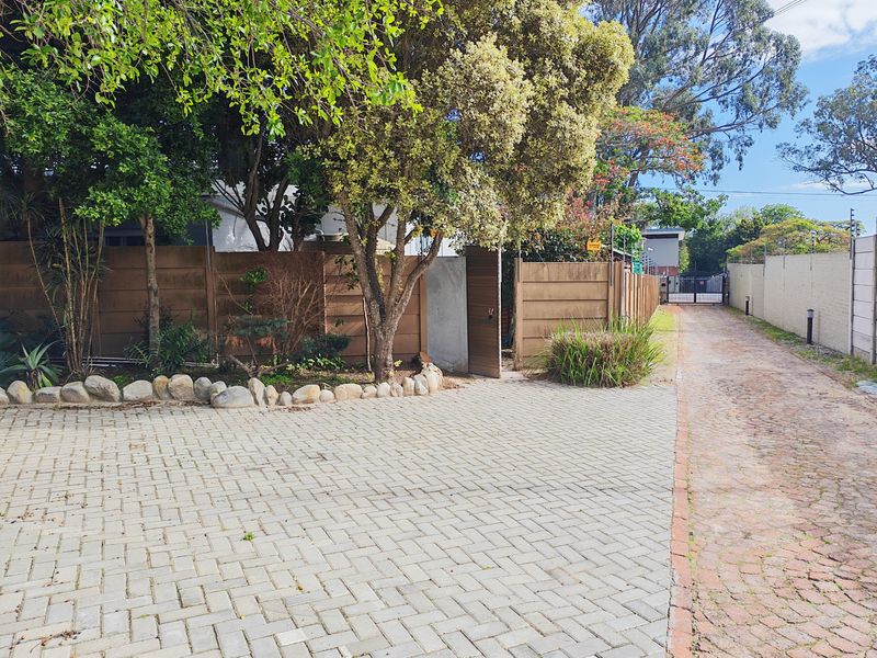 A paved driveway leading to a secure entrance, featuring boundary walls, established trees, and perimeter security fencing.