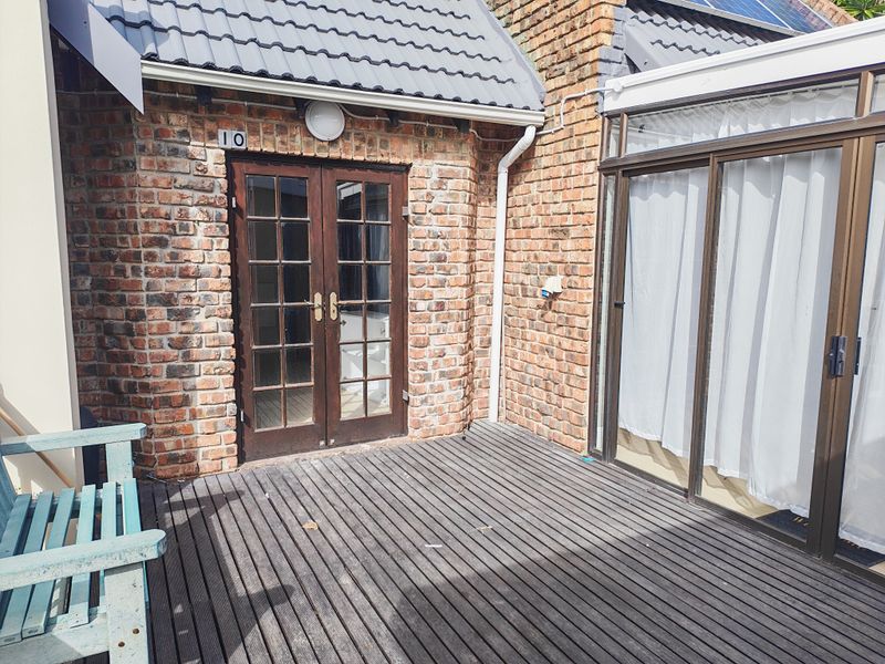 A private patio area featuring timber decking, exposed brick walls, and access via classic french doors and modern sliding glass doors.
