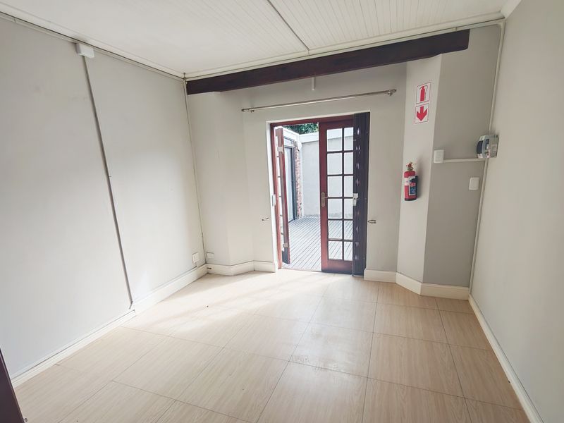 An empty living room featuring tiled flooring, an exposed timber ceiling beam, and a timber-framed glass door providing access to an outdoor area.
