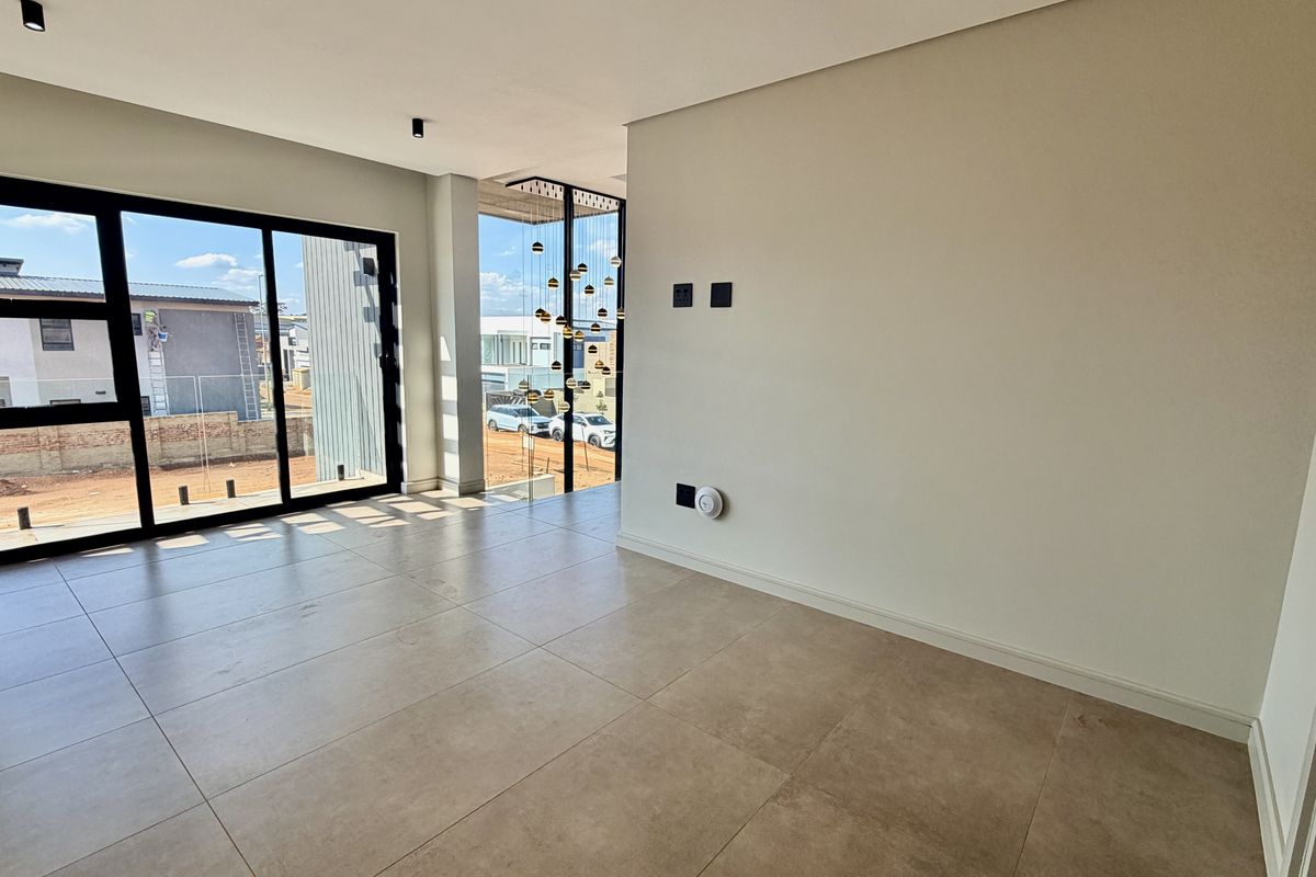 A bright, modern, and empty living area featuring large sliding glass doors, neutral tiled flooring, and contemporary pendant lighting.