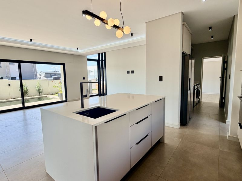 Modern open-plan kitchen featuring a central island with quartz countertops, sleek cabinetry, and seamless flow to the outdoor pool area.