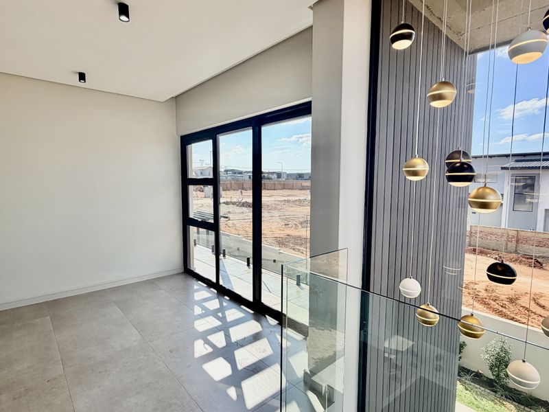 Modern, light-filled landing or hallway area featuring a glass balustrade, contemporary pendant lighting, and large format floor tiles with views over the estate.