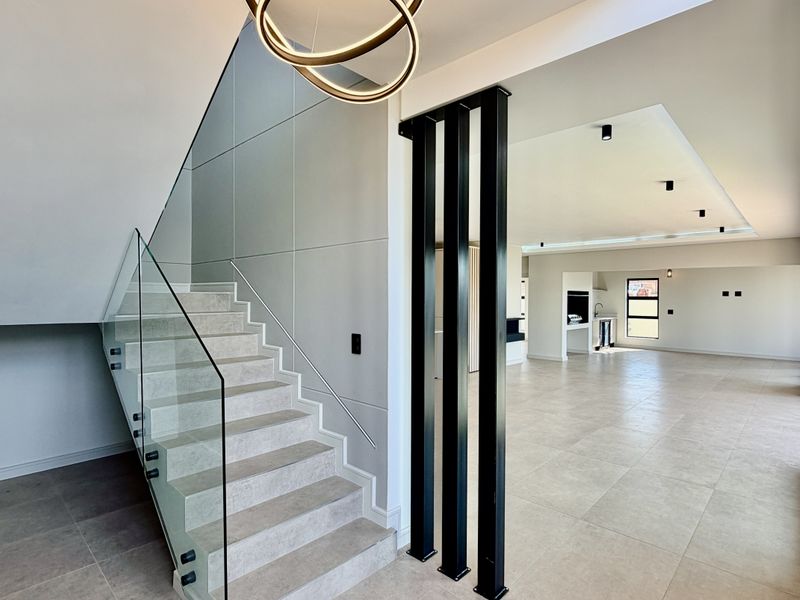 Spacious open-plan living area featuring a modern staircase with glass balustrade, neutral tiled flooring, and contemporary architectural lighting.