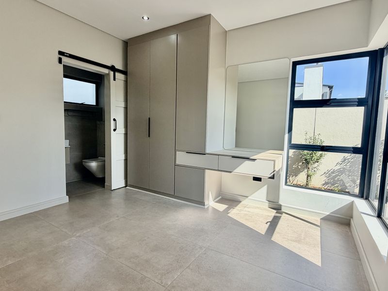 Modern bedroom featuring built-in cupboards, a floating vanity, tiled flooring, and an en-suite bathroom accessed via a sliding barn door.