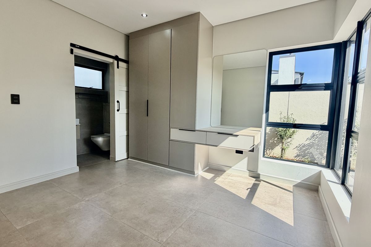 Modern bedroom featuring built-in cupboards, a floating vanity, tiled flooring, and an en-suite bathroom accessed via a sliding barn door.