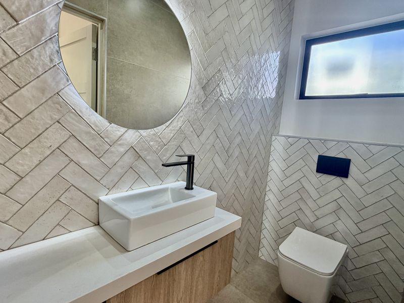 Modern bathroom featuring herringbone wall tiling, a sleek wall-mounted vanity with vessel sink, black fixtures, and a contemporary back-to-wall toilet.
