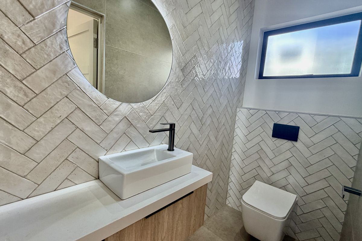 Modern bathroom featuring herringbone wall tiling, a sleek wall-mounted vanity with vessel sink, black fixtures, and a contemporary back-to-wall toilet.
