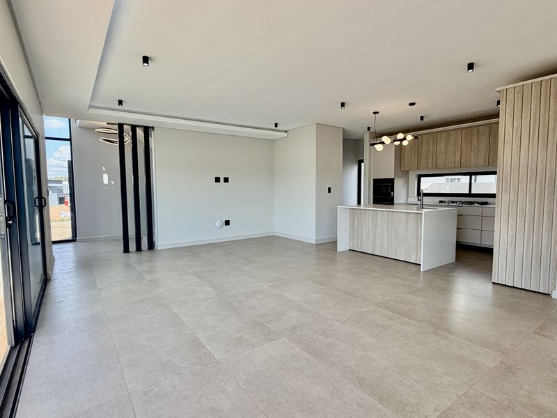 Spacious open-plan living and kitchen area featuring modern cabinetry, a central island, tiled floors, and large sliding doors leading to an outdoor patio.