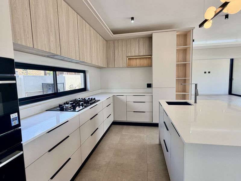 Modern kitchen featuring sleek cabinetry, stone countertops, a central island with a sink, and high-end built-in appliances in an open-plan layout.