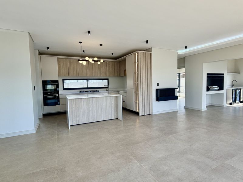 Spacious open-plan living area featuring a modern kitchen with built-in appliances, a central island, tiled flooring, and a built-in fireplace.