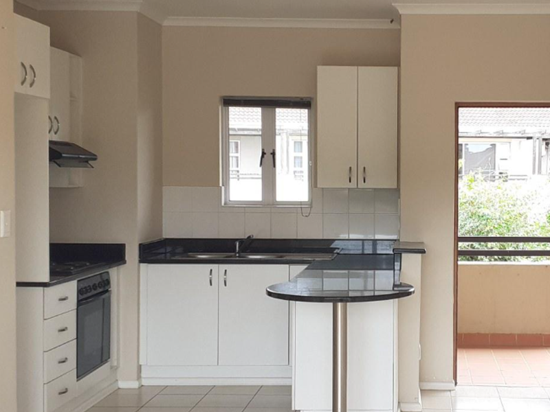 A clean, functional kitchen featuring white cabinetry, dark granite countertops, a breakfast bar, and integrated oven with extractor fan, leading out to a balcony.