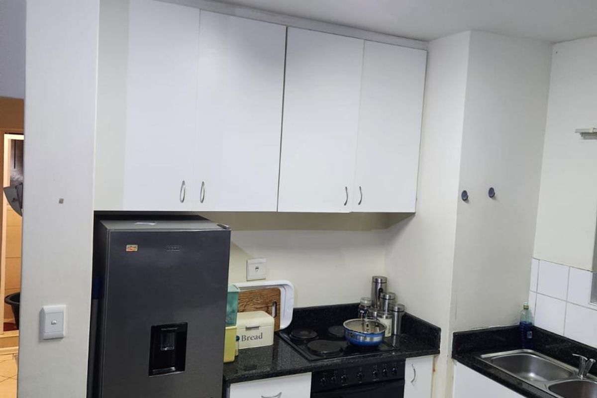 Compact kitchen featuring white cabinetry, dark granite countertops, built-in oven, electric hob, and a double bowl sink with tiled flooring.