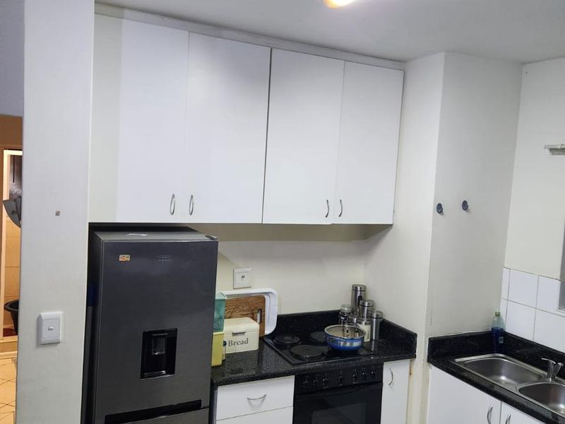 Compact kitchen featuring white cabinetry, dark granite countertops, built-in oven, electric hob, and a double bowl sink with tiled flooring.