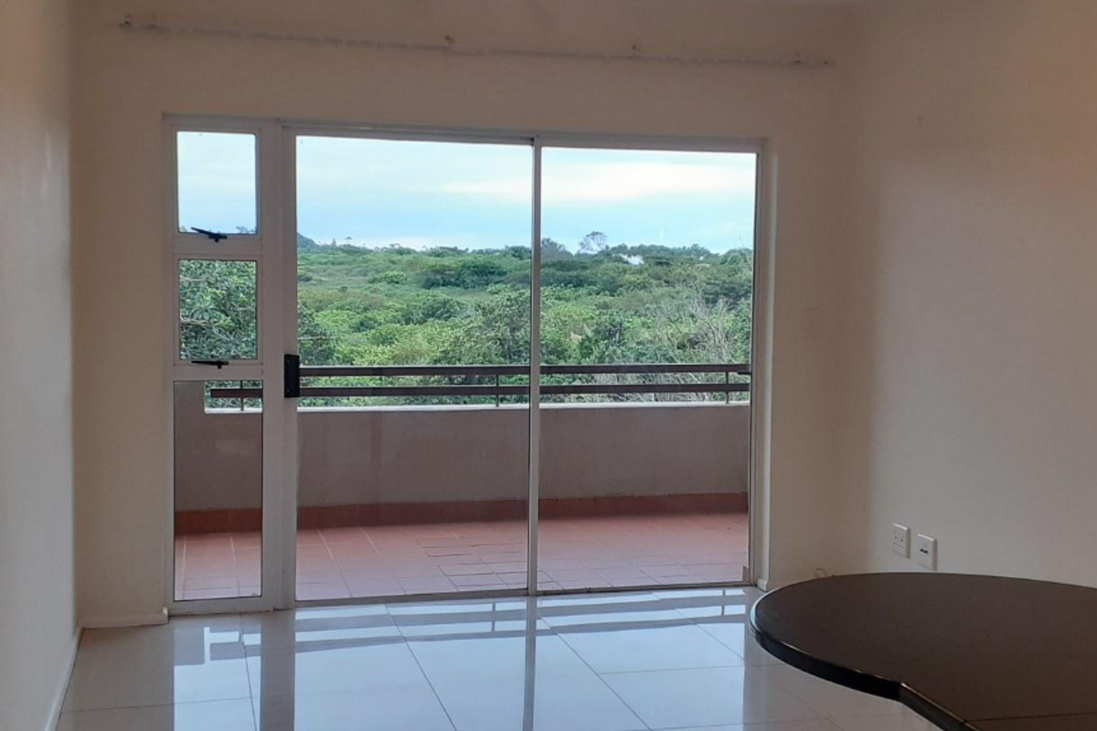 An empty living room featuring large sliding glass doors that open onto a balcony with scenic green views and tiled flooring throughout.
