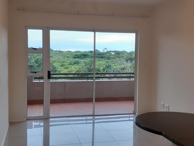 An empty living room featuring large sliding glass doors that open onto a balcony with scenic green views and tiled flooring throughout.