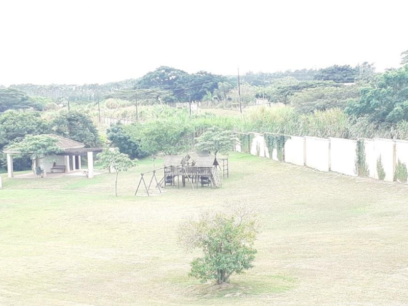 A spacious communal garden area featuring a large lawn, perimeter boundary wall, and a covered gazebo structure.