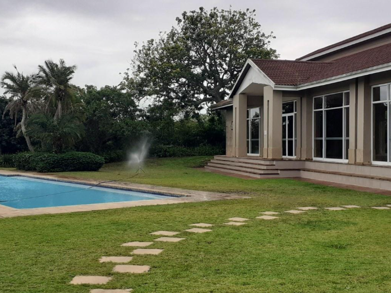 A spacious rear exterior view featuring a swimming pool, landscaped lawn with stone pavers, and a building facade with large glass windows.