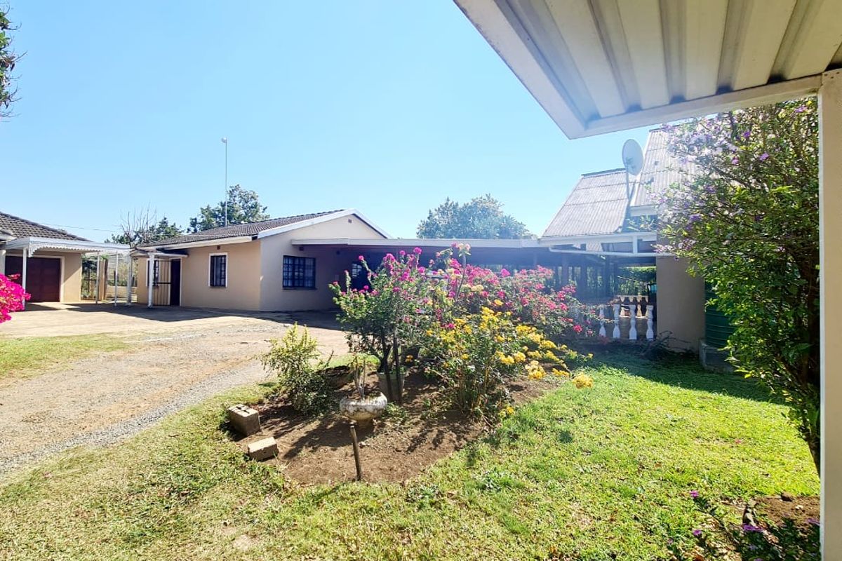 A view of the property exterior featuring a gravel driveway, landscaped garden beds, and covered patio area under a corrugated roof.