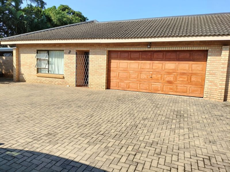 Front exterior view of the apartment featuring a brick facade, tiled roof, paved driveway, and a wooden garage door.