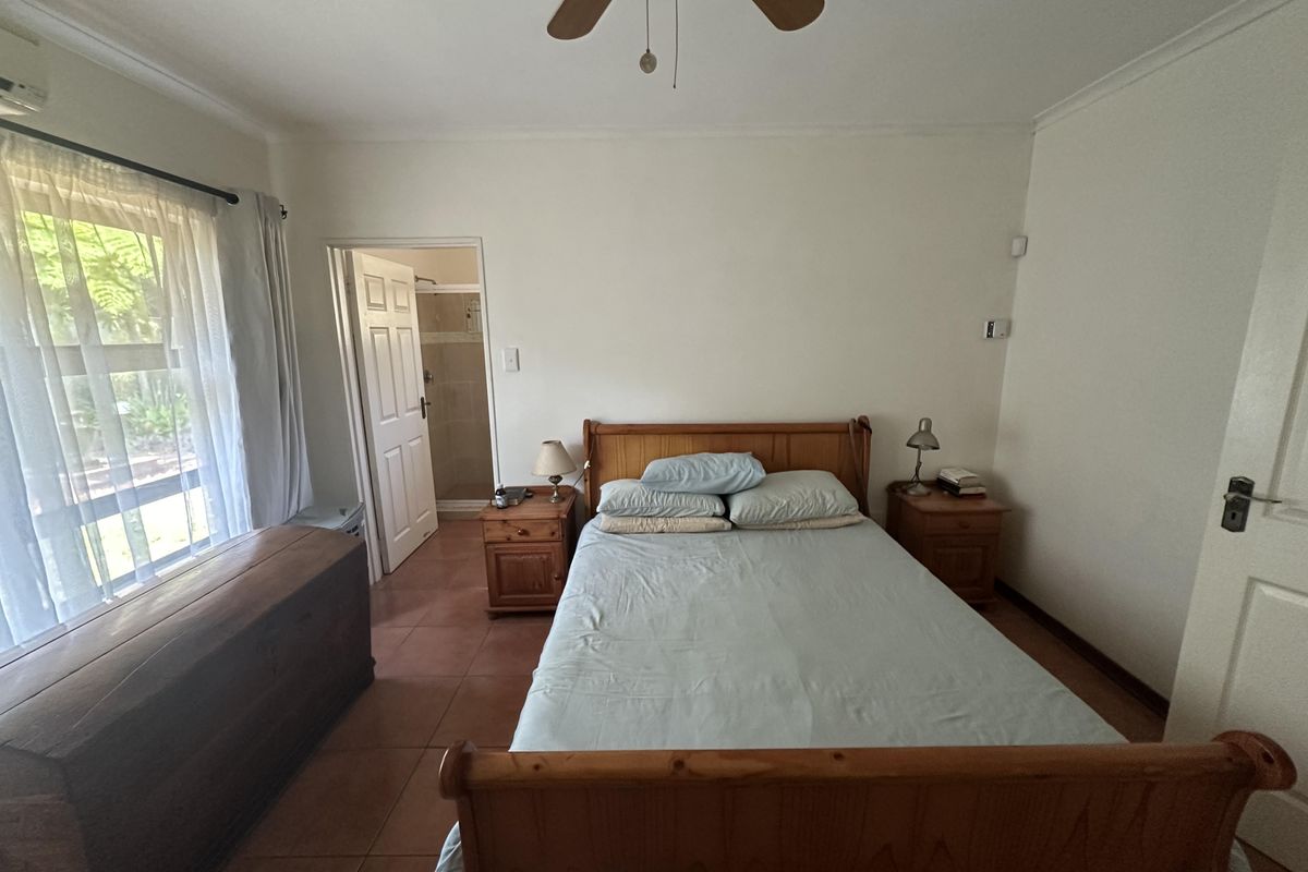 A bedroom featuring tiled flooring, a ceiling fan, an air conditioning unit, and direct access to an en-suite bathroom.