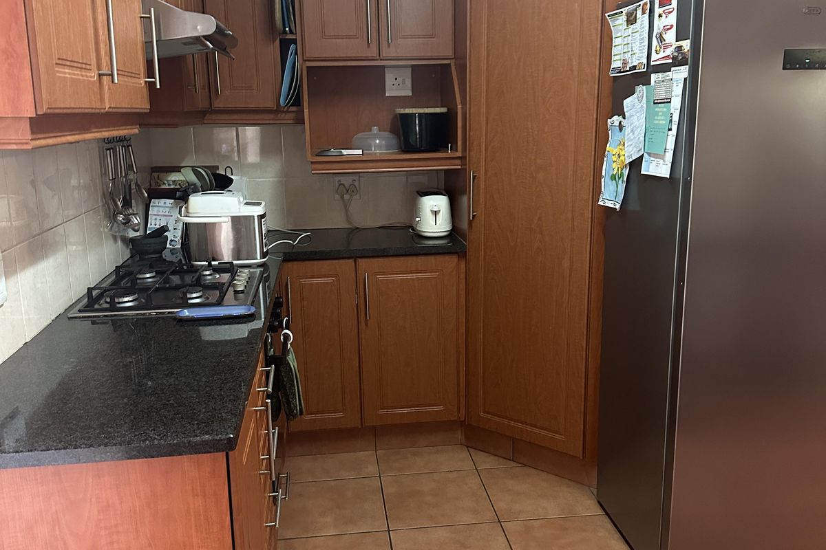 Functional kitchen featuring wood-look laminate cabinetry, granite countertops, gas hob with extractor fan, and durable tiled flooring.