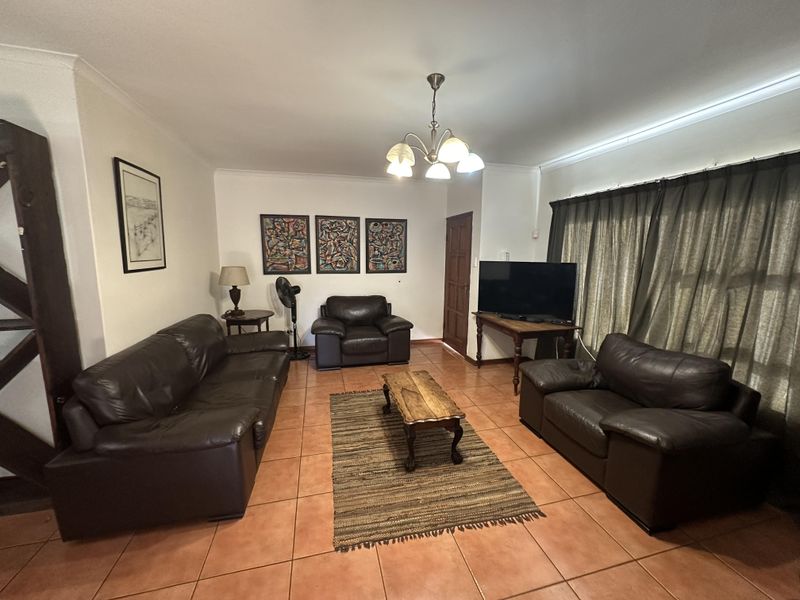 A spacious living room featuring ceramic floor tiles, cove cornicing, and a central light fixture, offering a comfortable and functional layout.