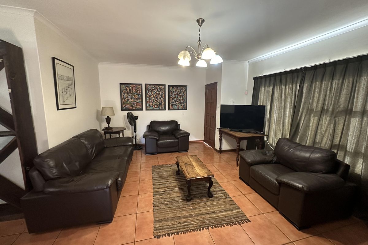 A spacious living room featuring ceramic floor tiles, cove cornicing, and a central light fixture, offering a comfortable and functional layout.