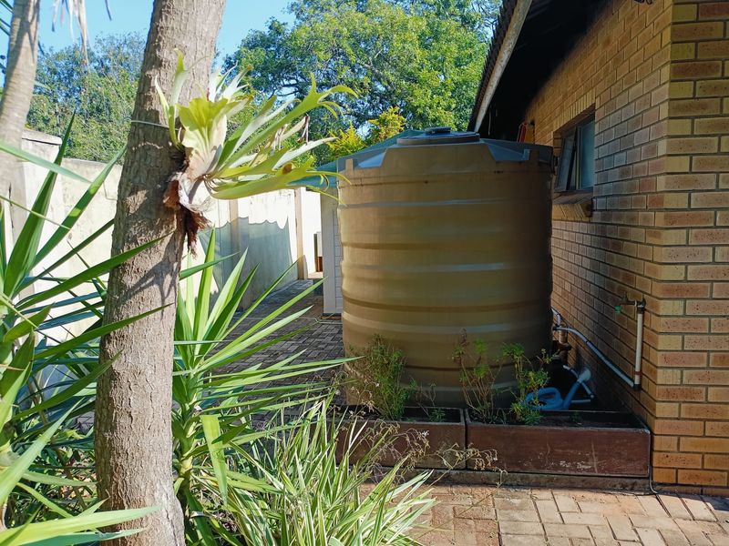 A side exterior view of the property featuring a large water storage tank positioned against a brick wall on a paved surface.