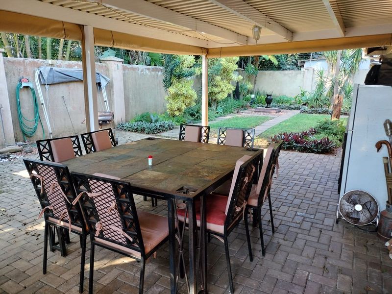 A covered outdoor patio area featuring paved flooring, overlooking a private garden with established landscaping and boundary walls.