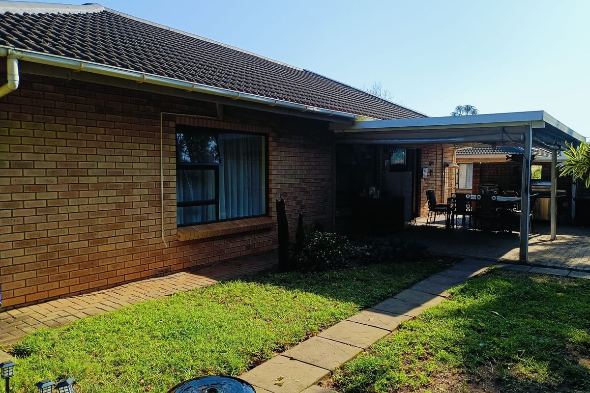 Rear view of the apartment featuring a brick facade, tiled roof, and a covered patio area overlooking a small garden with a paved walkway.