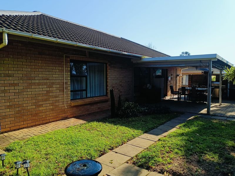 Rear view of the apartment featuring a brick facade, tiled roof, and a covered patio area overlooking a small garden with a paved walkway.