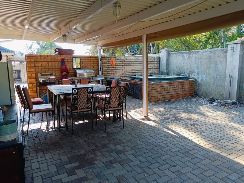 Covered outdoor patio featuring paved flooring, a built-in braai area, and a built-in spa, providing a functional space for outdoor entertainment.