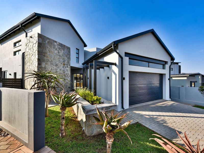 Modern double-story residential facade featuring stone cladding, a paved driveway, and an integrated garage with clean architectural lines.