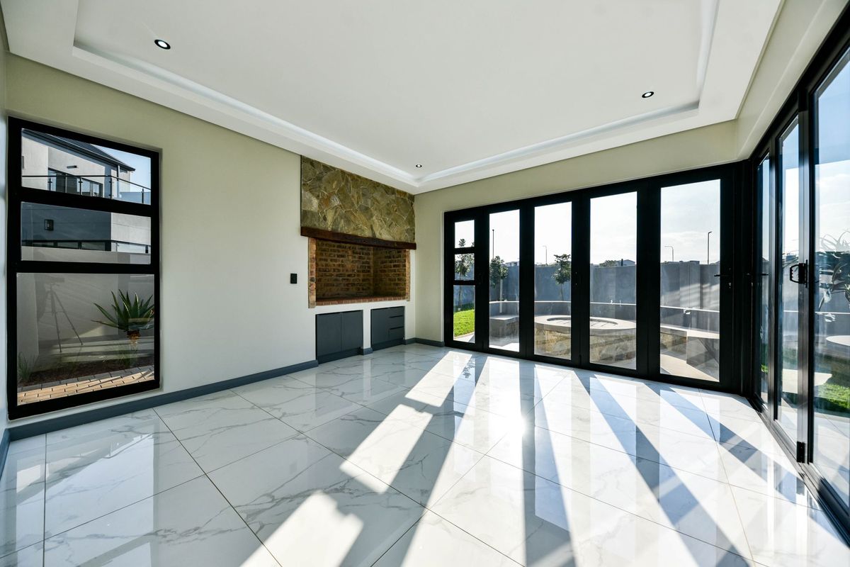 A bright, modern living room featuring large black aluminium stacker doors, marble-look floor tiles, and a built-in fireplace with stone cladding.