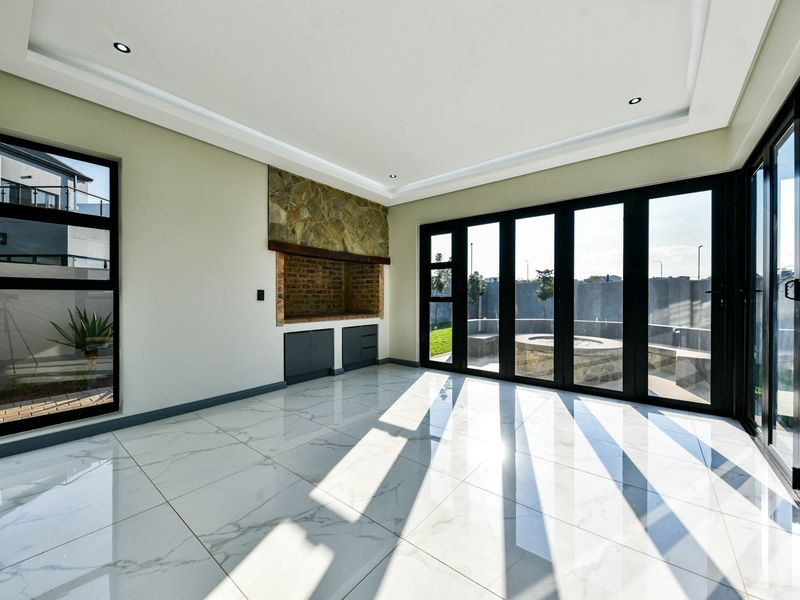A bright, modern living room featuring large black aluminium stacker doors, marble-look floor tiles, and a built-in fireplace with stone cladding.