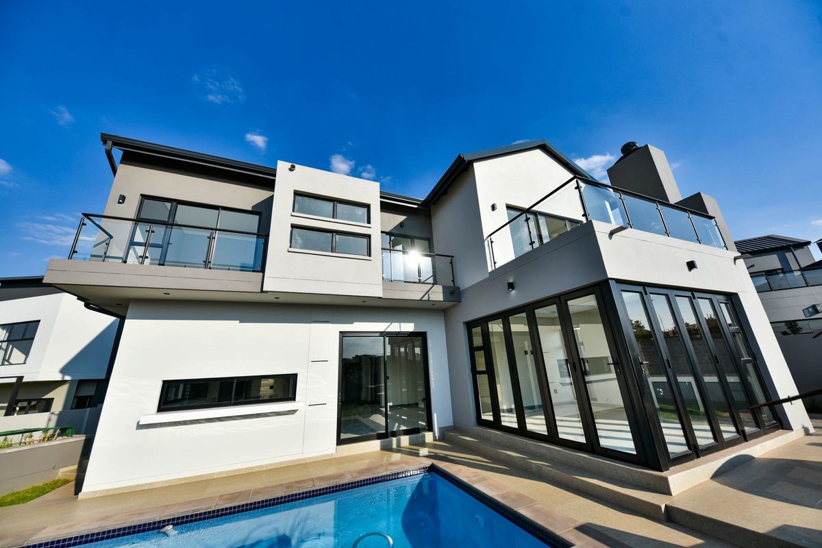 Modern double-storey rear elevation featuring a swimming pool, expansive glass bi-fold doors, and upper-level balconies with glass balustrades.
