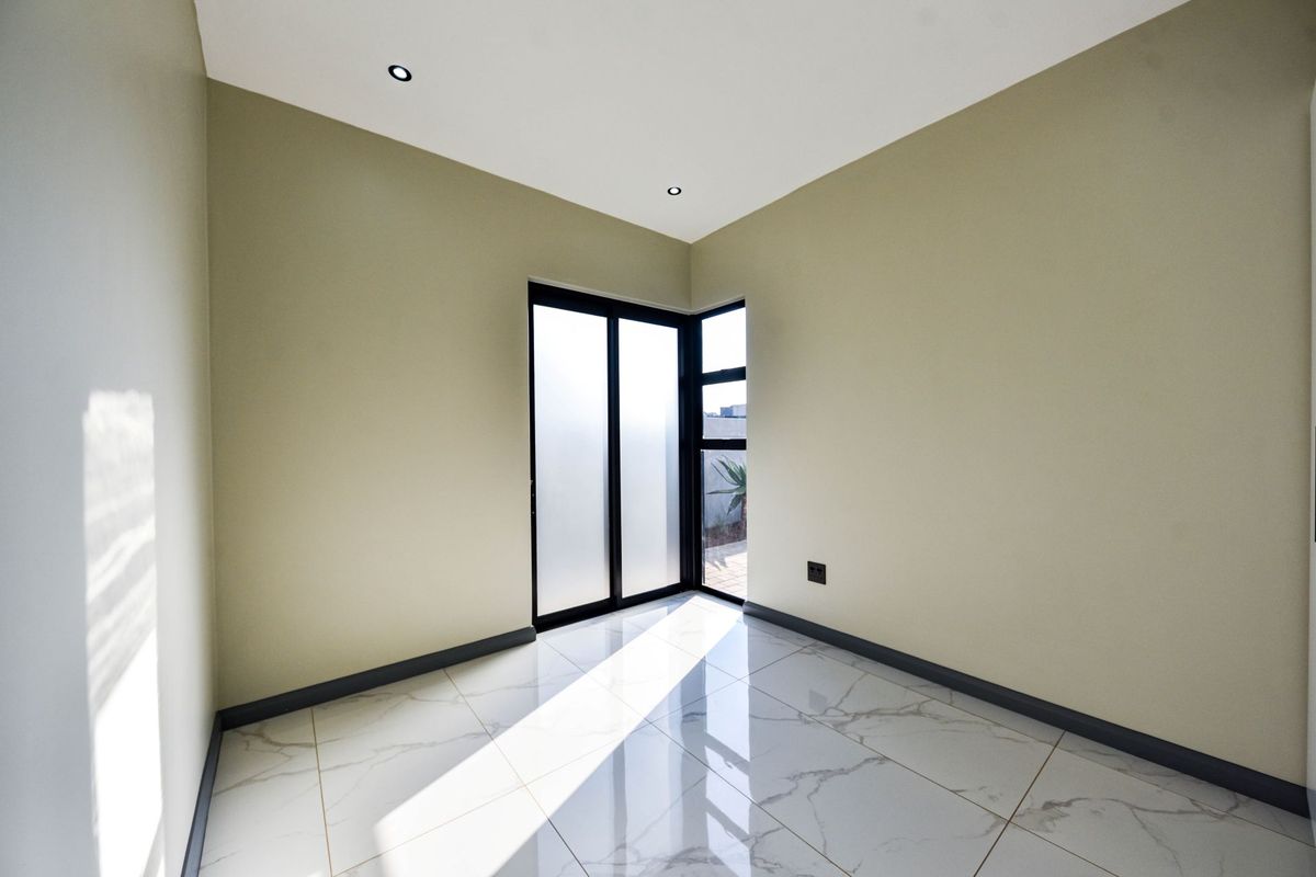 A bright, empty bedroom featuring modern marble-look floor tiles, recessed downlights, and black aluminium corner windows providing natural light.