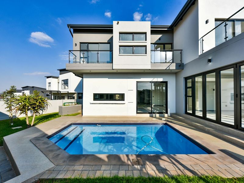 Modern double-story home exterior featuring a private swimming pool, paved patio area, and upper-level balconies with glass balustrades.