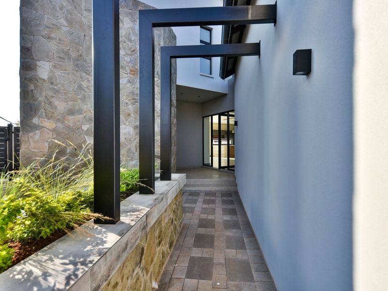 A modern entrance walkway featuring stone cladding, a paved path, and a striking black metal pergola structure leading to the main entrance.