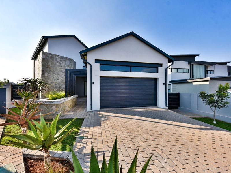 Modern front elevation featuring a paved driveway, double garage, stone cladding accents, and well-maintained landscaping.