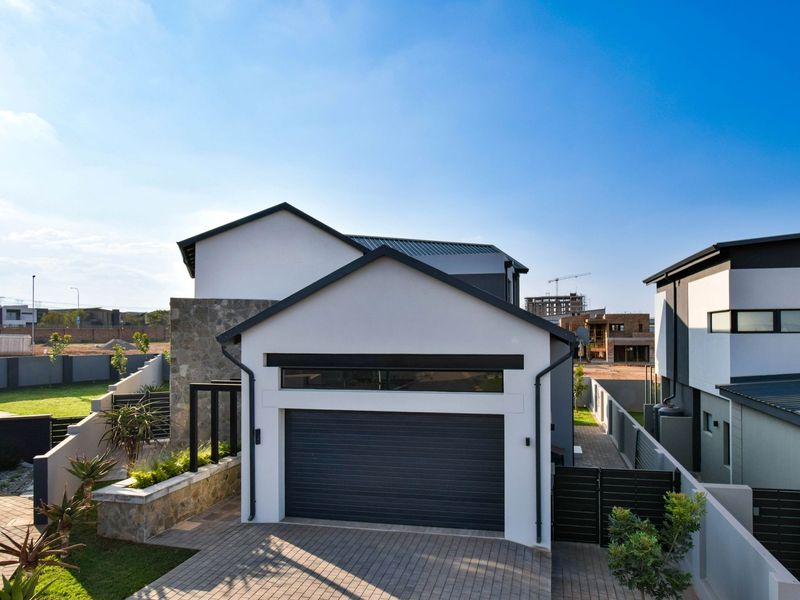 Modern residential exterior featuring a paved driveway, automated garage door, and stone cladding accents, set within a contemporary estate environment.