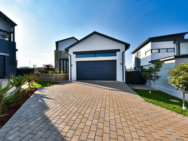 Modern residential front elevation featuring a paved driveway, automated garage door, stone cladding accents, and well-maintained landscaped garden areas.
