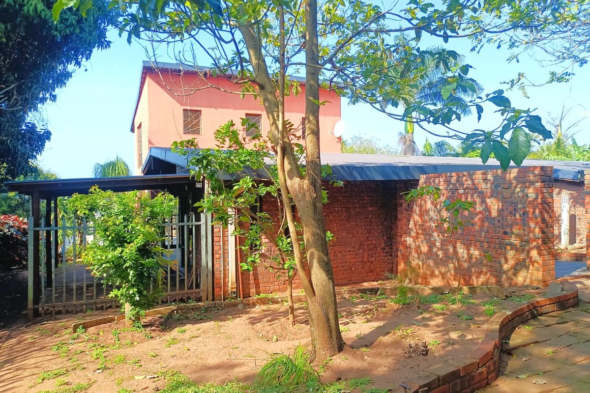 Rear view of the property featuring face brick exterior walls, a covered patio area, and a garden space with established trees and brick edging.