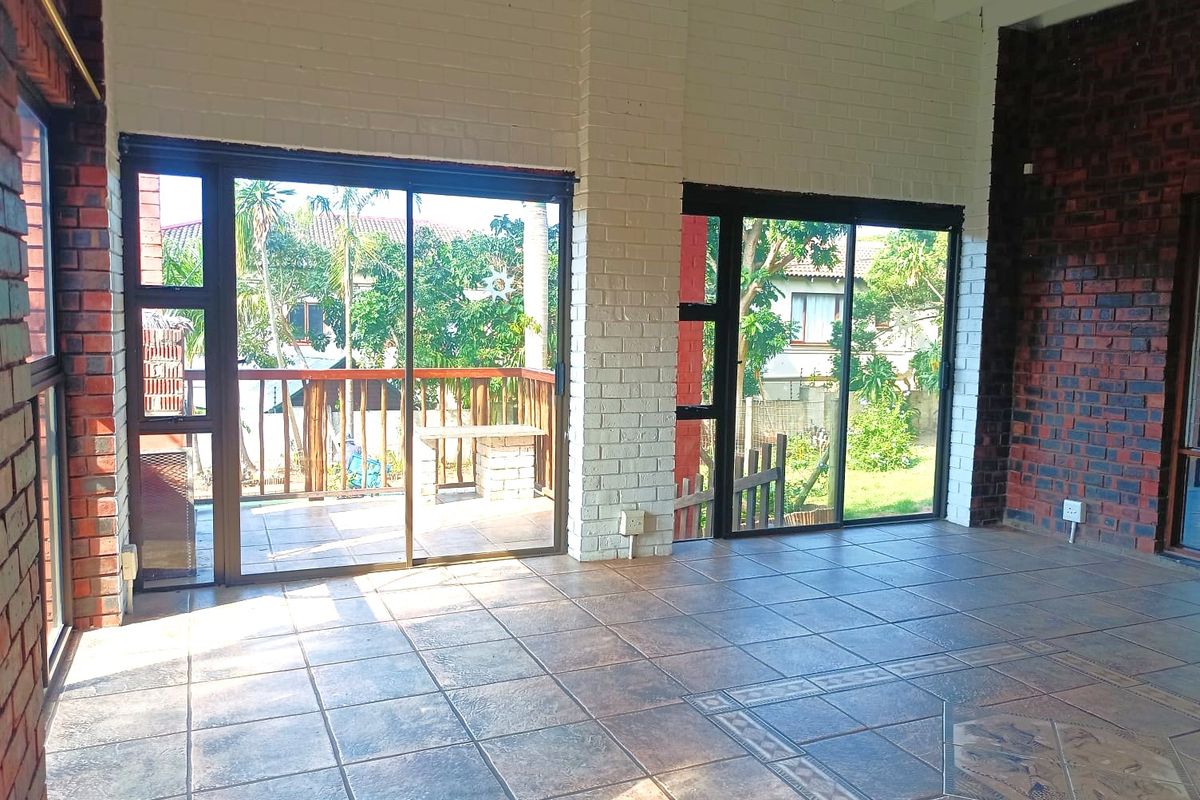 Spacious living area featuring tiled floors, exposed brick walls, and large sliding glass doors providing natural light and access to the outdoor patio.