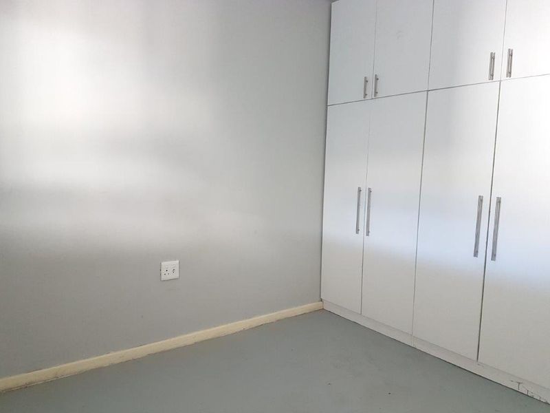 A clean, empty bedroom featuring neutral grey walls and ample built-in cupboard storage with modern handles.