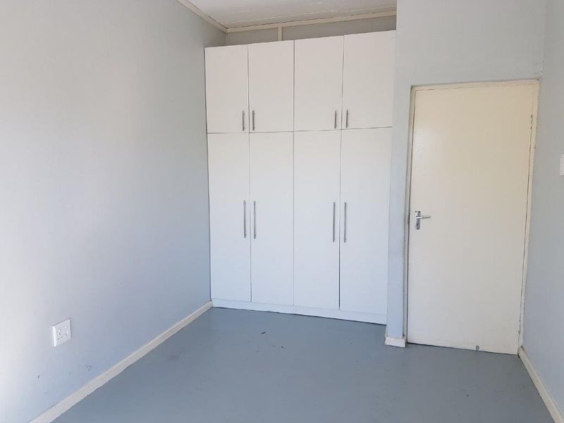 A clean, empty bedroom featuring built-in white cupboards and neutral wall finishes, providing a versatile space ready for personalization.