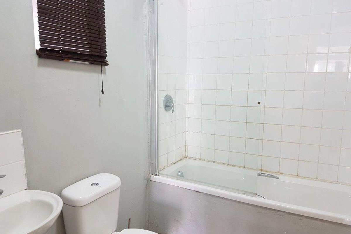 A functional bathroom featuring a bathtub with a glass shower screen, pedestal basin, and toilet, requiring some cosmetic updates to the grout and paintwork.