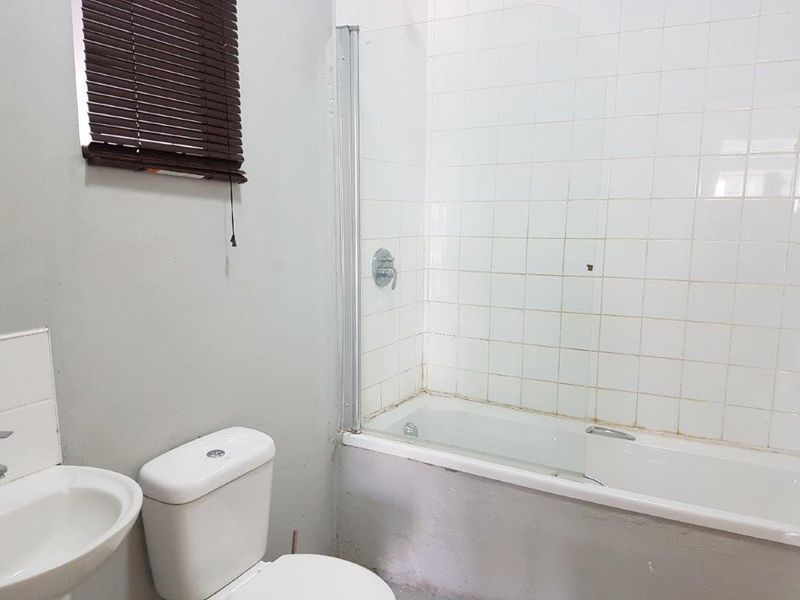 A functional bathroom featuring a bathtub with a glass shower screen, pedestal basin, and toilet, requiring some cosmetic updates to the grout and paintwork.